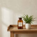 Flora Feed No. 01 amber glass bottle of liquid plant food beside fern on oak bench