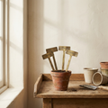 Aged Brass Plant Markers stamped brass stakes in terracotta pot on oak potting bench