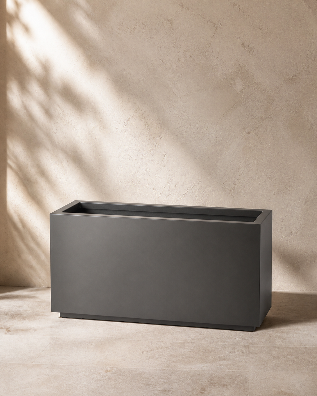 Charcoal long box outdoor planter in a warm limestone studio.