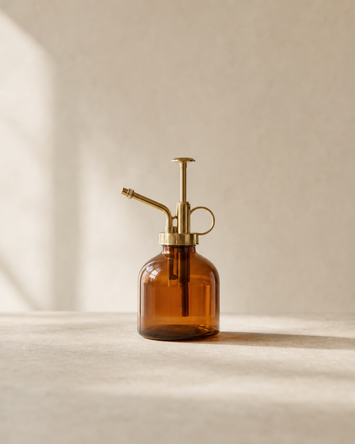 Amber glass mist bottle with brass sprayer on pale limestone.
