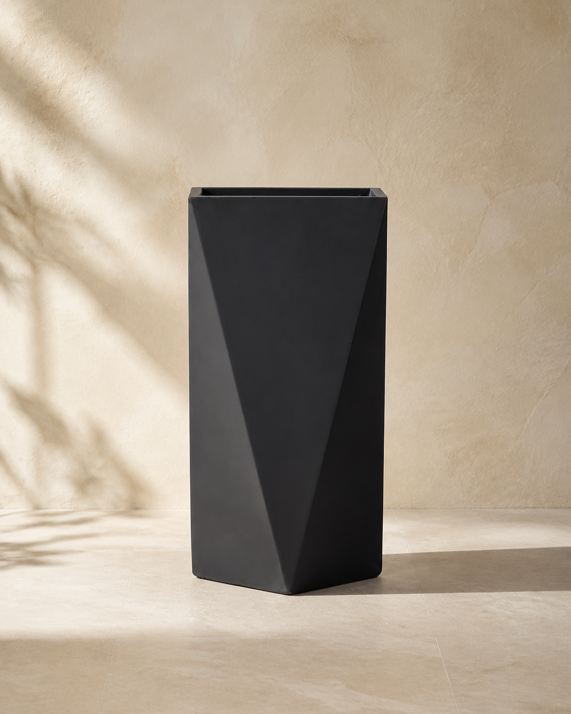 Black angular faceted cement planter in a warm limestone interior.