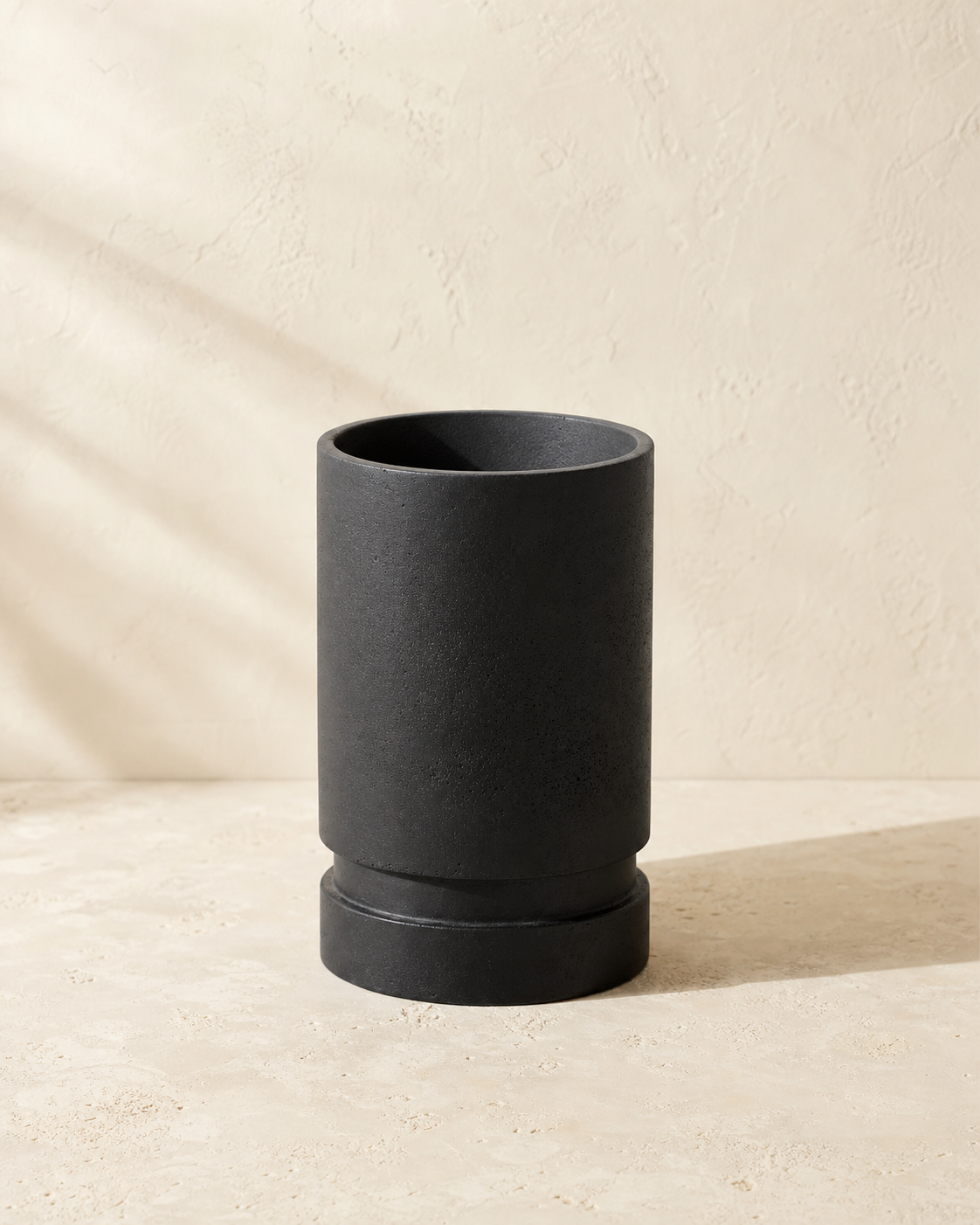 Argo matte black tiered round planter in a warm limestone studio.