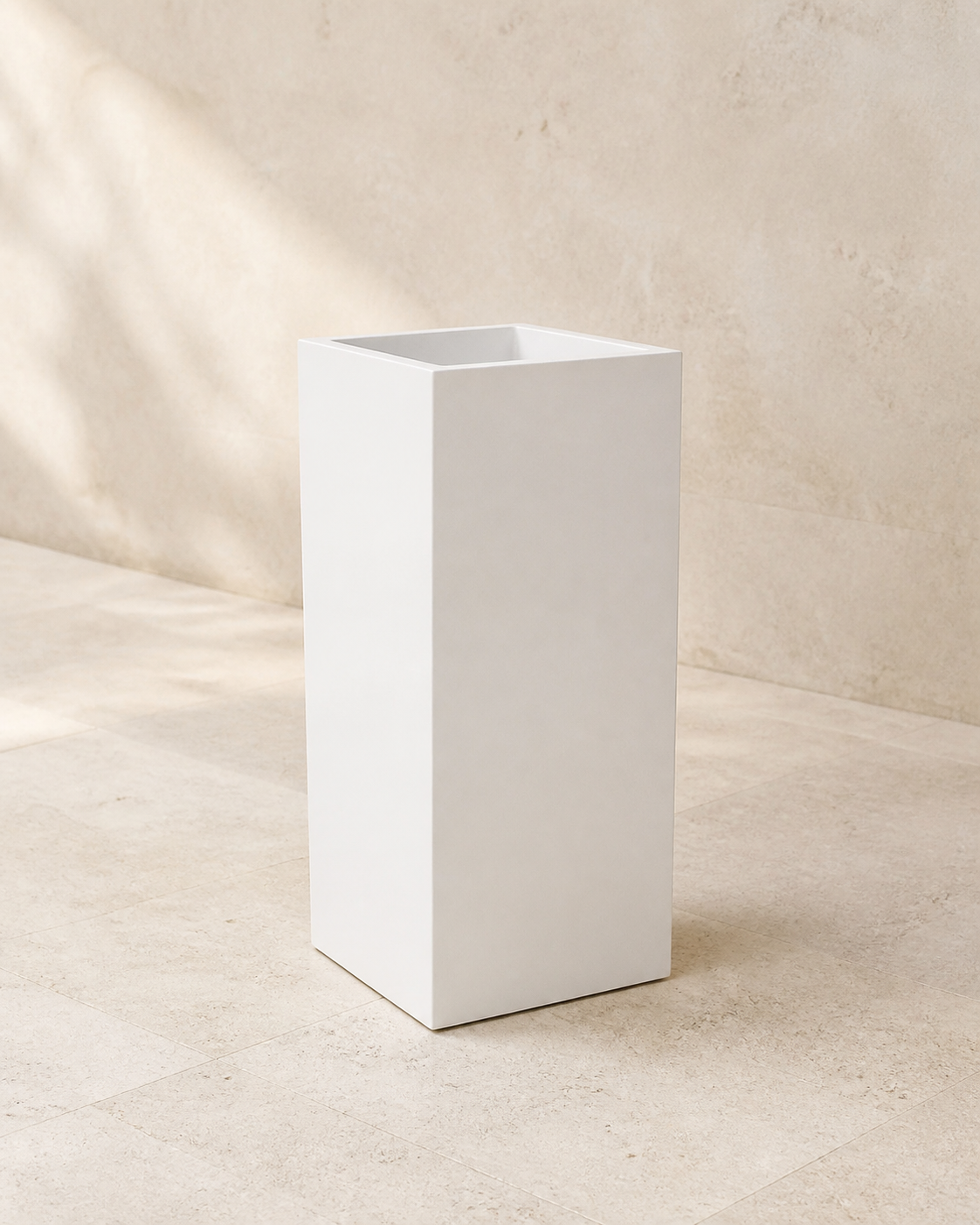 White square pedestal outdoor planter in a warm limestone interior.