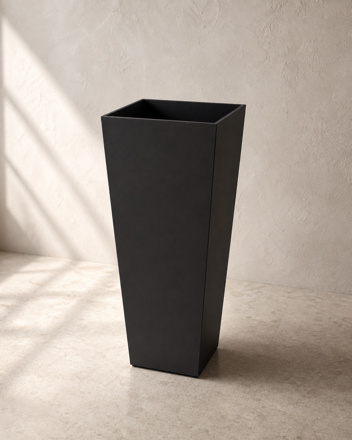 Black tapered tall Hevea outdoor planter against warm limewashed plaster.
