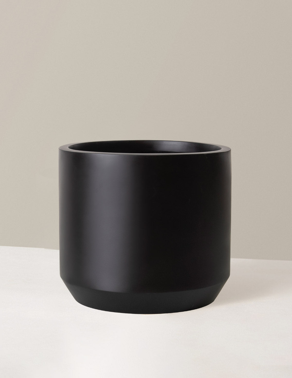 Black cylindrical planter on a beige background
