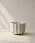 Angled view of the Dune Wrap Planter showing its fluted profile on a warm-neutral limestone surface.