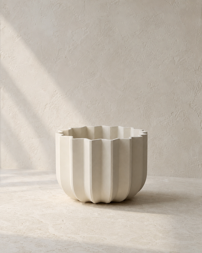 Angled view of the Dune Wrap Planter showing its fluted profile on a warm-neutral limestone surface.